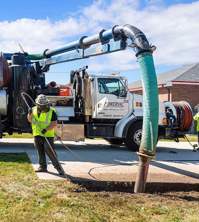 A worker operates a vacuum truck during an outdoor maintenance task.