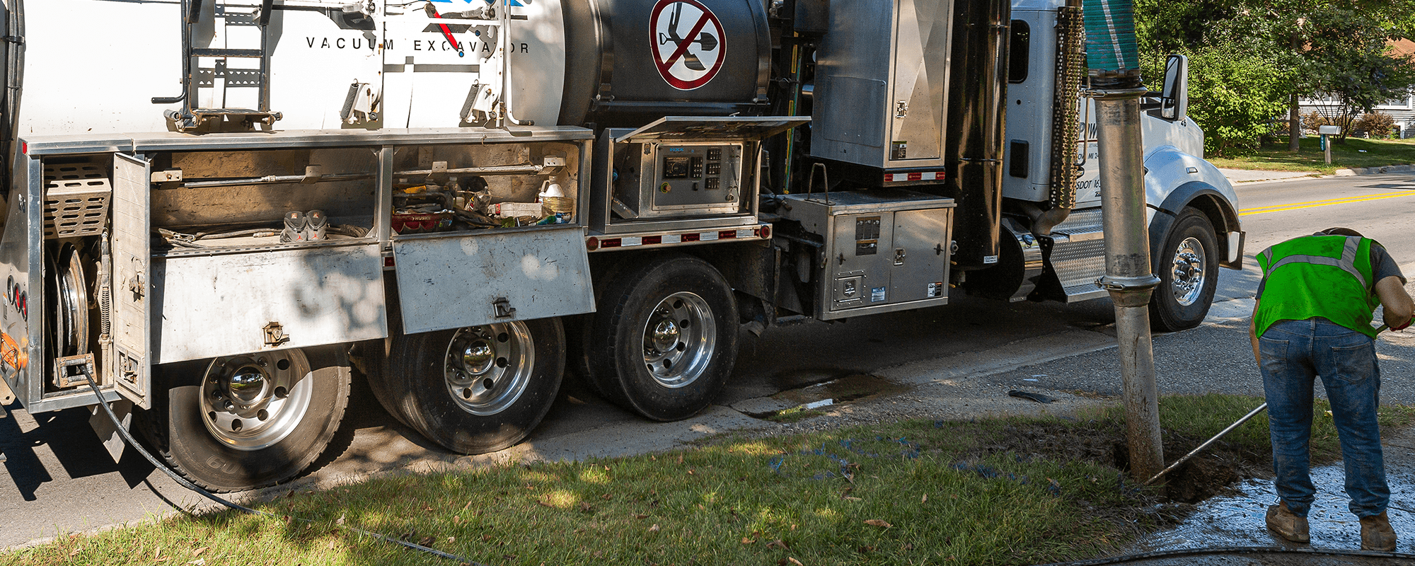 A utility worker operating a vacuum excavator truck on the roadside.