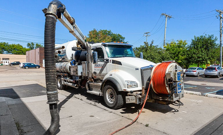 Vacuum truck with large hoses in parking lot on a sunny day.