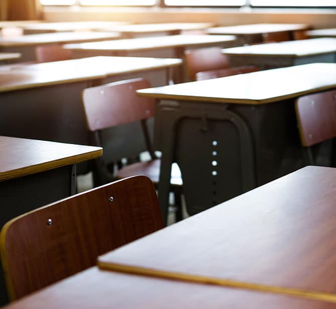 Empty classroom with rows of wooden desks and chairs in sunlight.