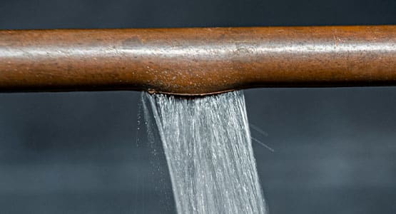 Water leaking from a rusty pipe against a dark background.