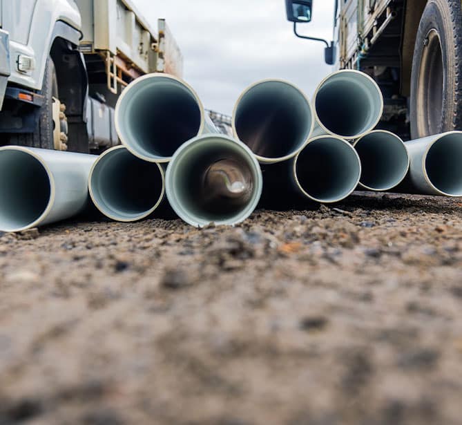 Pipes stacked on a construction site with trucks in the background.
