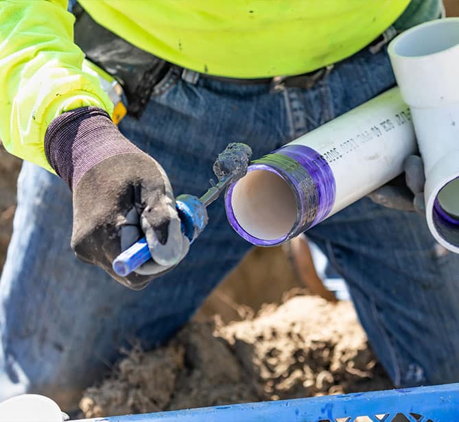 A person applying adhesive to PVC pipe for plumbing work.