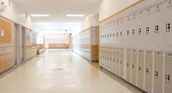 Empty school hallway with rows of lockers on one side and classroom doors on the other.