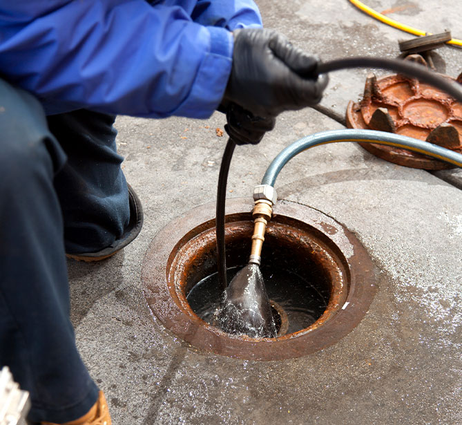 A person cleaning a drain with a high-pressure hose and gloves on a concrete surface.