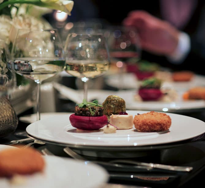Gourmet meal on white plate with wine glasses at a dinner table.