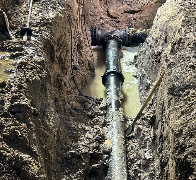 A large pipe installed in a muddy trench, surrounded by wet soil and tools.