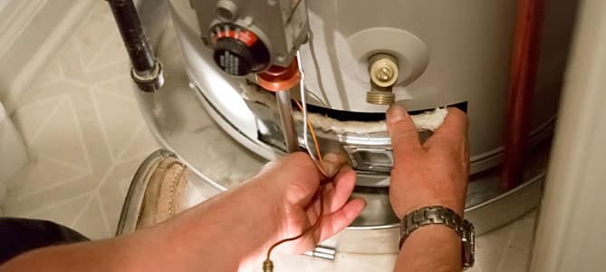 Person repairing a water heater, adjusting components.