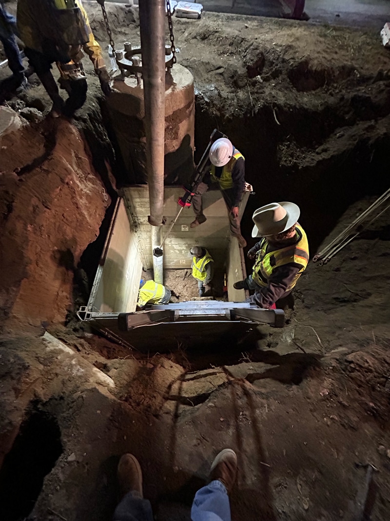 Construction workers installing a large pipe underground at a worksite.
