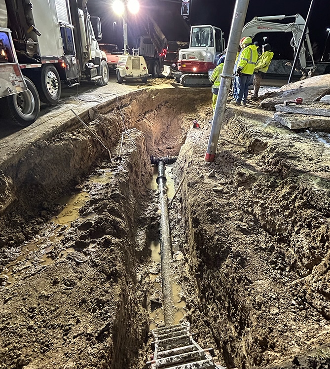 Construction site at night with workers, trench, and excavators preparing for pipeline installation.