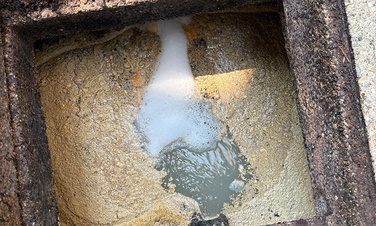Grease trap filled with solidified waste and water, viewed from above.
