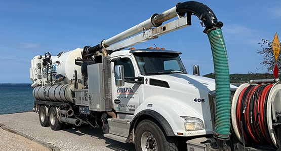 Vacuum truck parked by a lakeside with blue sky.