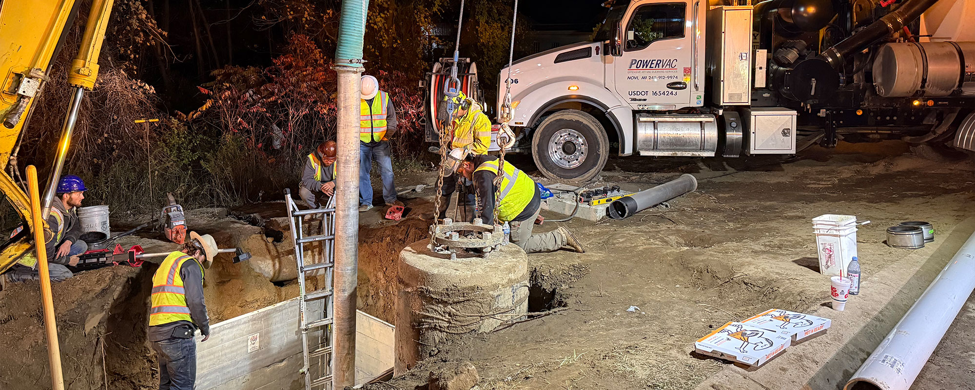 Construction crew working at night near a utility truck and digging equipment.