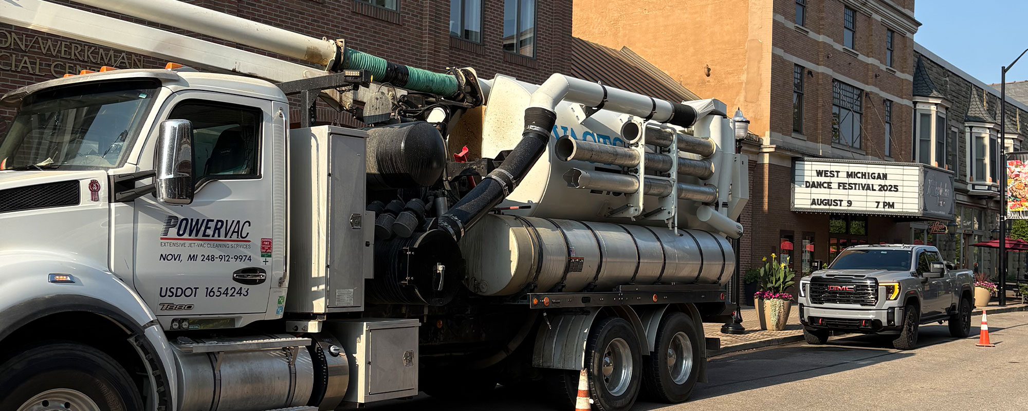 Vacuum truck parked on a street near a building with a festival sign.