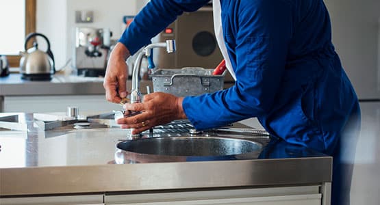 Person in blue overalls repairing a kitchen sink faucet.