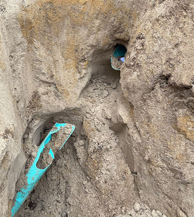 Broken blue pipe in sandy soil with visible damage.