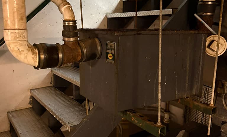 Industrial plumbing system with metal pipes and machinery near stairs.