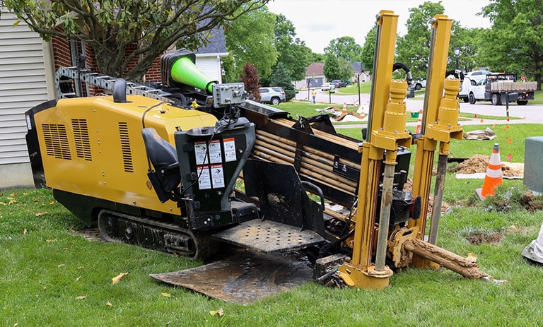 Yellow directional drilling machine operating near a house.