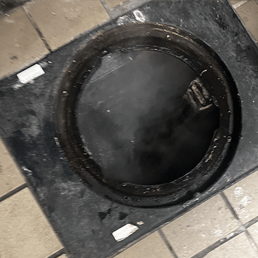 Steaming manhole on a tiled floor emitting vapor.