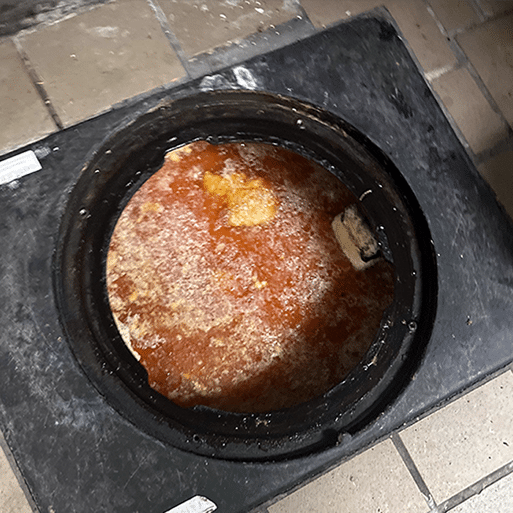 Open sewer manhole filled with reddish water and debris.